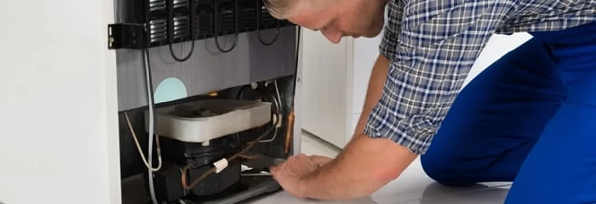 Refrigerator repair technician servicing the compressor and condenser area in Indianapolis, IN